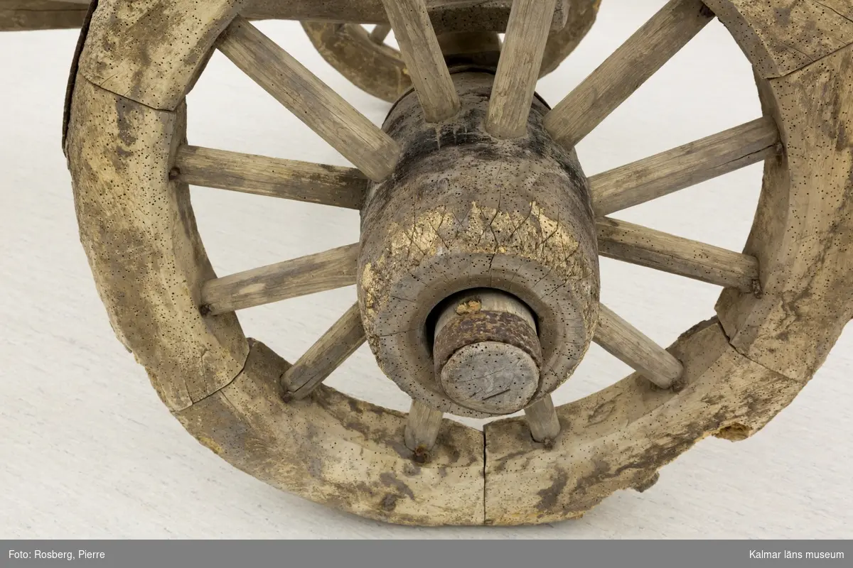 KLM 11833. Bultvagn, hästvagn. Av trä och järn. För hästar. Bultvagn som består av två hjulpar med två bankar, fyra träaxlahjul med järnbeslag, skakel samt dräkt. Det främre hjulparet är mindre än det bakre och har en tillhörande skakel som fästes i en träanordning på dess bank. Dräkten består av en kraftig rektangulär stång av trä med sex stycken borrade hål. Dräkten fästes i en annan träanordning som sitter på motsatt sida av skakeln på det främre hjulparets bank. På det bakre hjulparets bank sitter ett bågformat hål där dräkten sedan förs igenom för att sammankoppla vagnens delar samt justera dess längd. De bakre hjulens nav är dekorerade med zig-zag mönster.