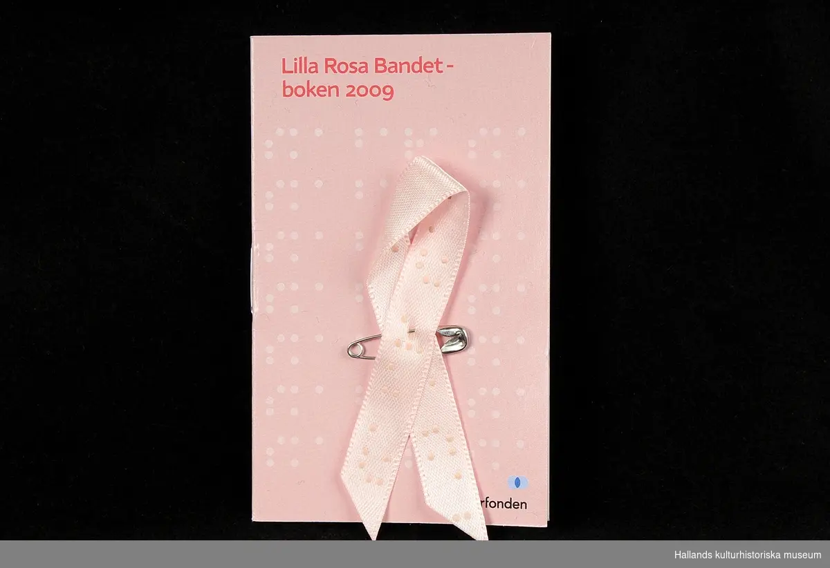 Fem stycken rockmärken, i form av "Rosa Bandet". Rosa "sidenband" vikt och sammansatt med liten säkerhetsnål. Bandet och en liten textbok ligger i en plastficka. Utvalda formgivare ger bandet varierat utseende varje år. 
a) 2006, Carin Rodebjer(trasmatta). b) 2007, Lars Wallin(kedja). c) 2008, Ingegerd Råman (text). d) 2009, Gert Wingårdh (blindskrift). e) 2011, Lena Ph, Per Holknekt (omfamning).