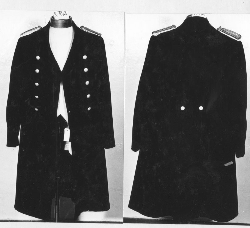 Rock, modell 1878 av mörkblått kläde. För vice krigsdomaren vid Karlskrona örlogsstations krigsrätt.
Rocken har tillhört rådman F W Flensburg, Karlskrona, som 8/1 1926 blev vice krigsdomare.
Den är försedd med epåletter av vitt tyg, på vilkas översida finns en träns av guldtråd och därovan ett svärd av silver.
Rocken är dubbelknäppt med knappar av förgylld mässing som i sin tur är försedda med en lilja och ett svärd i relief. I ryggen finns två liknande knappar.