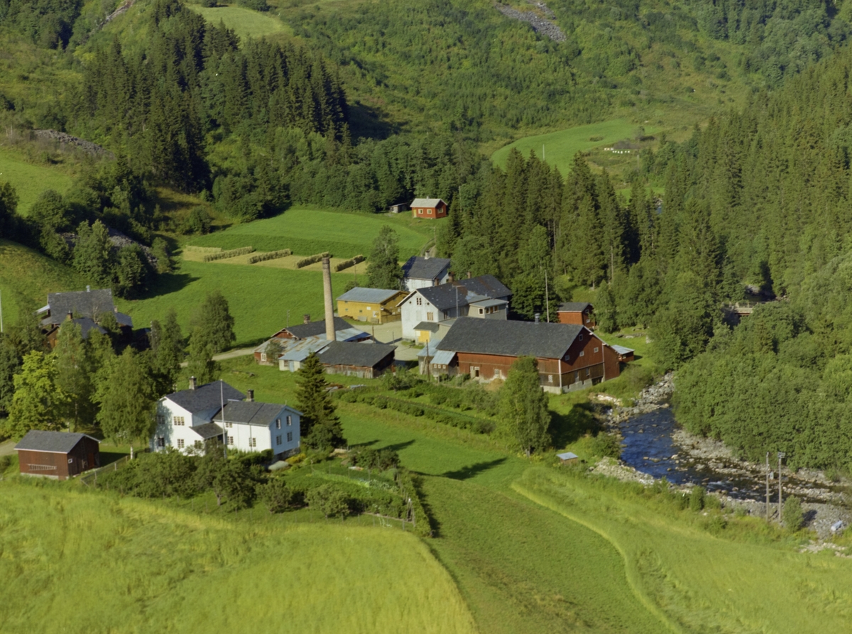 Landhandleri, Gardsbruk, Frøysesetra. Bruvang. Østre Gausdal.(Tidligere ysteri) Hvitt hus med hage og flaggstang i forgrunn samt kornåker. Lave lagerbygninger med høy pipe, stor rød lagerbygning, landhandleri i stor. toetasjes bygning. Mindre gul bygning i midten med hesjer på jorde i bakgrunnen. Flekkevis skog og Gausa til høyre.