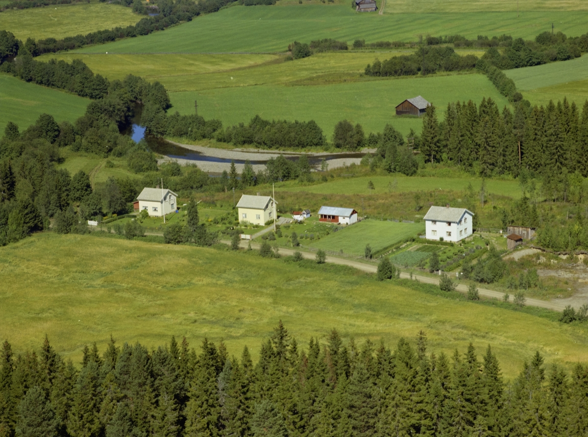 Lybu. Småhusbebyggelse. Tre hvitmalte hus med bær-og grønnsakhager.  Åkrer. Granskog. Elv.