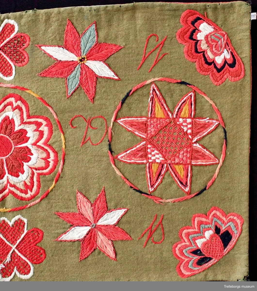 Bottentyg är grön vadmal. Tre stora ringar i kontur utgör huvudmotiv. I ringen i mitten är en stor blomma med 8 kronblad utfyllnad. I de båda ringarna vid sidan är broderat en spetsuddig stjärna med 8 vingpar. Dess centrum är en snedställd kvadrat, sydd i gallerliknande konstsöm. Utmed agedynans långsidor är broderat olika blomsterstjärnor, pionliknande blommor och en blomliknande rundning av 4 st hjärtfigurer. Färger: vitt, gult, svart, blågrått samt många olika nyanser i rött. Baksidan tegelröd yllevävnad. 
Enligt katalogen märkt I.W.D.S.  SL. Hjärtrosetter och hjärtan. 
Enligt Ernst Fischer, Årsbok från Malmö museum 1971, sid 180: En åkdyna i Tbgs museum har som mittmotiv en runduddig stjärna, omgiven av en ring samt en hjärtrosett över och under, flankerad av spetsuddiga stjärnor. T.h. och v om mittmotivet stora spetsuddiga stjärnor inom ringar. I hörnen varierande blomformer. De ganska svårtydda initialerna skulle kunna tydas som LWD IVH, ehuru bokstäverna då icke är placerade i rätt ordning. IVH skall i så fall beteckna I Vämmenhög.