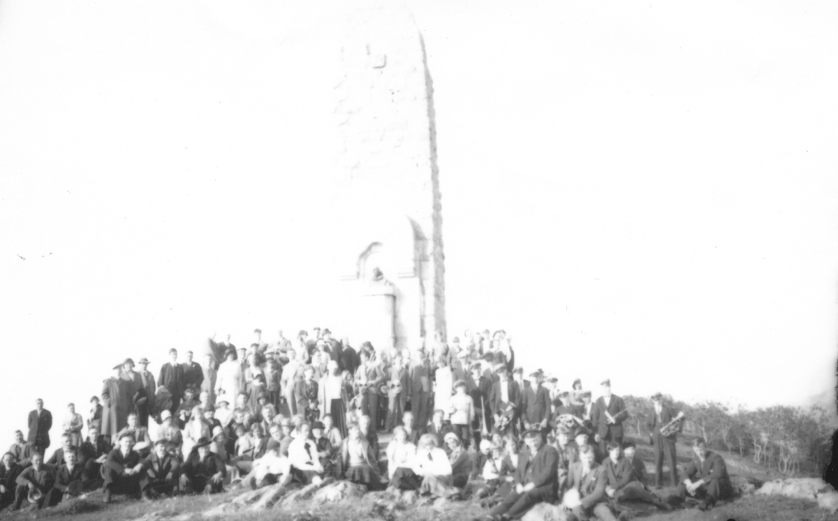 Gruppe mennesker foran en høy statue. Petter Dass-bautaen i Alstahaug.