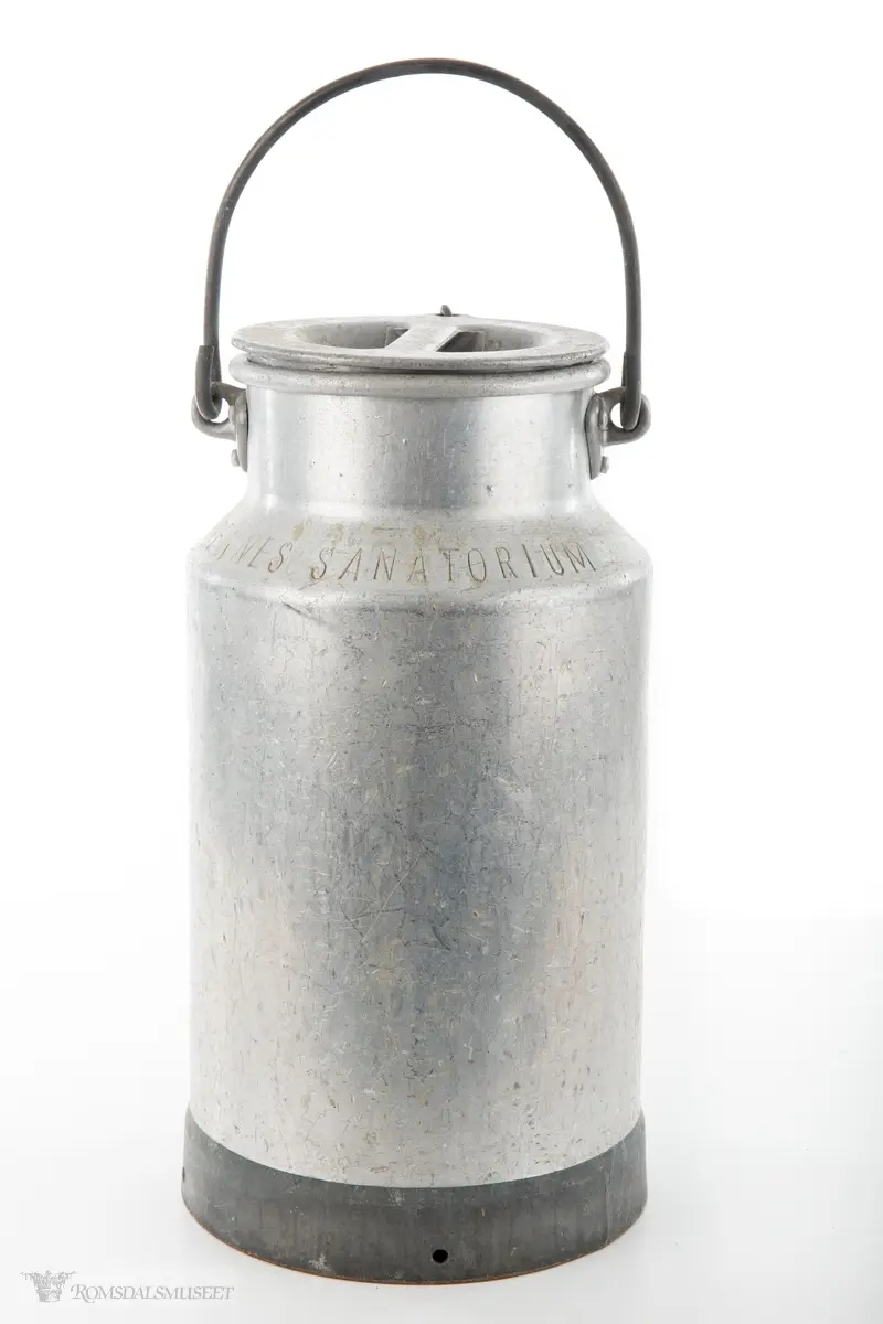 Melkespann i aluminium med lokk og hank. Lokket er festet i spannet med kjetting. Spannet har forsterket bunn.