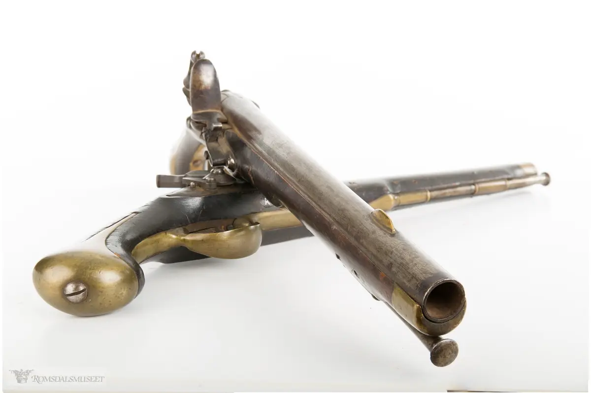 Flintlåspistol med glattboret løp, uten baksikte og med åpent korn. Skjefte av bøk med messingbeslag i enden og ved munningen. To røkner med ladestokk.