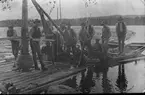 En samling män, på en ev. timmerflotte.