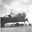 Närbild. Amerikanska bombflygplanet Boeing B-17 Flying Fortress står på ett flygfält. I bakgrunden står en folksamling.