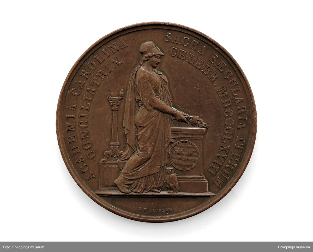 Medalj av kopparlegering, åtsida: Karl XV i högerprofil med text runtom, " CAROLUS XV REX SVECIAEN ET NORVEGIAE". Frånsida: allegorisk kvinnogestalt med lagerkrans och uggla (= Pallas Athena/ Minerva) invid en sockel med tre kronor i en cirkel och en oljelampa (?) på en liten kolonn; inskription:  ACADEMIA CAROLINA SACRA SAECULARIA ITERUM CONCILIATRIX CELEBR. MD CCCLXV III samt gravörens namn, J. Ericsson.