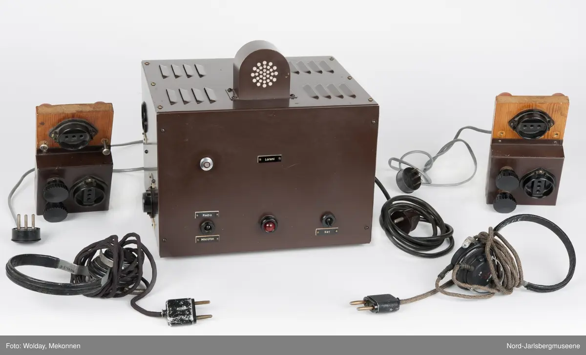 Brun metallkasse med lufterister på høyre kortside og topp. front med reguleringsknapper og hjul, rød lampe, og uttak. Elevapparater har to reguleringshjul og er montert på treplater som er koblet sammen med forsterkeren med ledning og kontakt, og til øretelefonene med ledning i kontakt. Øretelefonene er av bakelitt, metall og lær.
Sort bakelitt også på elevapparatene.


5 deler tilsammen