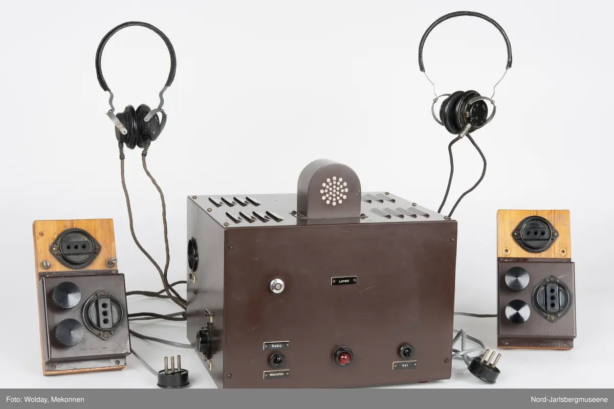 Brun metallkasse med lufterister på høyre kortside og topp. front med reguleringsknapper og hjul, rød lampe, og uttak. Elevapparater har to reguleringshjul og er montert på treplater som er koblet sammen med forsterkeren med ledning og kontakt, og til øretelefonene med ledning i kontakt. Øretelefonene er av bakelitt, metall og lær.
Sort bakelitt også på elevapparatene.


5 deler tilsammen