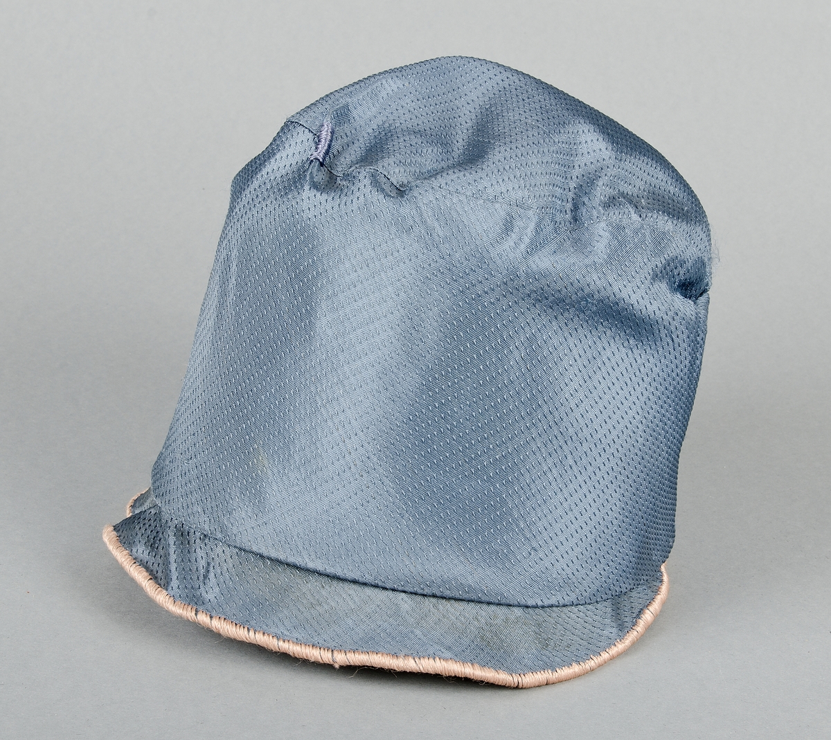 Damhatt av blått mönstrat siden med applikationer i ljusbrunt siden och broderier med blått och ljusbrunt silke. Skärmen fodrad med samma tyg som applikationerna. Fodrad med vitt tyg. Vit prislapp med svart text.