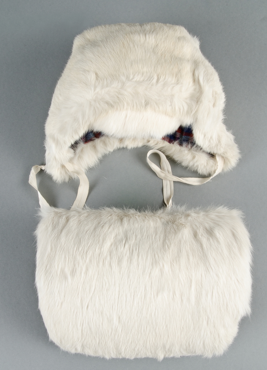 Muff med vitt kaninskinn på framsidan och grå sammet på baksidan, ficka med blixtlås på baksidan. Fodrad med vit bomullslärft, stoppad. Ingen hängband.