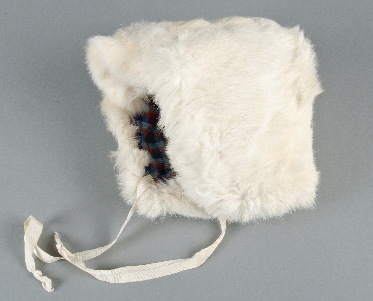 Muff med vitt kaninskinn på framsidan och grå sammet på baksidan, ficka med blixtlås på baksidan. Fodrad med vit bomullslärft, stoppad. Ingen hängband.