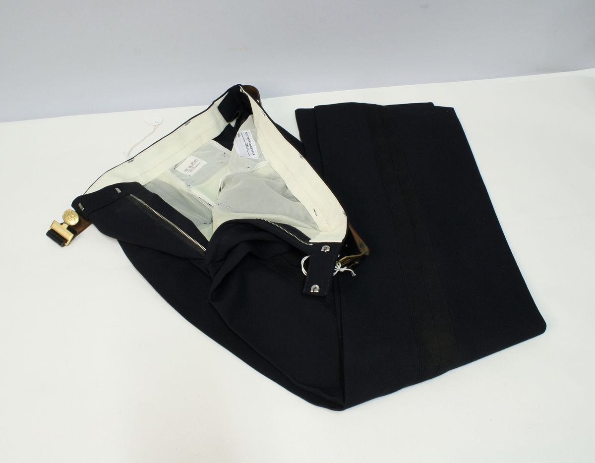 Uniform for politinspektør etter 1963-reglement med merking etter 1977-reglement. Helårsuniform M/1963 med skjorte, langbukse, belte, helårskappe og jakke. Skyggelue med gullbrodert bånd, loslue og båtlue M/1967. Kappen og jakken har skulderklaffer av flettede gullsnorer med to sølvstjerner og festeknapp i gullbroderi. Skjorten har en enklere skulderklaff med to gule render og to sølvstjerner. Det følger med et ekstra enkelt lærbelte og et ekstra sett skulderklaffer til skjorte. Plaggene har gullfargede løveknapper.