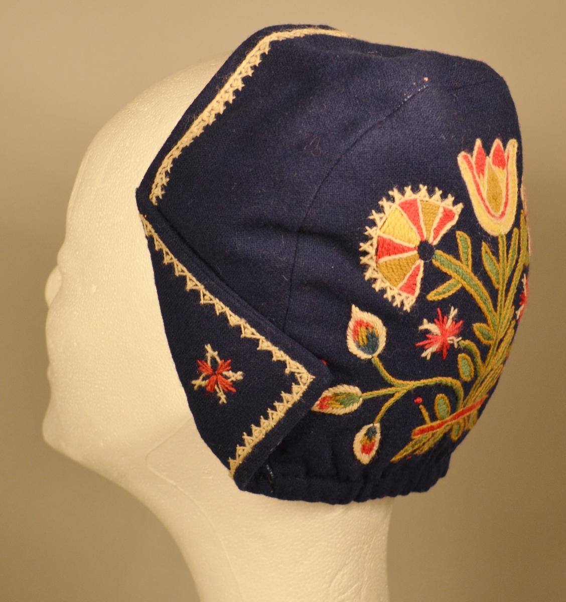 A: Bunad. Blått ullstoff, tynn klede. Har ein brodert bord 5 cm frå nedre kant. Brodert i ullgarn. Borden er 33 cm bred og går rundt same høgde. Det er en grenbord med blomster sydd i plattsøm, kontursting og franske knuter. Overdelen er eit skjørteliv. Rundt skjørtet er det brodert ein bord i kvit snorsøm, fiskebeinsting og franske knuter. Bak 3 stjerner i røde og kvite, foran på skjøtene 4 stjerner. Den broderte kvite borden fortsetter foran og opp og rundt halslinning. Foret overdel med lysgrå silke. 8 sølvringer foran i åpningen for sølvkjede. Denne bunaden har nedsydde folder frå 5 cm og opp til 8,5 cm lengde (ikkje vanleg). Splitten i skjørtet er satt saman med to trykknapper og ein hekte, og overdelen er satt saman i livet med to hekter. Skjørtet er festet til overdelen ti steder. Overdelen går i spiss ned bak.

B: Lue
Maken stoff og broderi som bunad. På pullen er det brodert eit tre med blomster. Same broderi som på overdel er brodert foran på luen. Foret med lysegrå silke. Kyse fasong. H: 17,5 cm, B:18,8 sm

C: Veske
Same stoff og broderi som bunad. Lås i messing. Same for. Låsen påsydd for hand. Låsen er merket: 
JONS KRISTIANSEN
KJOSE
NN
Veske med lås, total lengde: 28,7 cm, bredde: 16,4 cm

D: Skjorte
Kvit bomull med nuppereller. Halslinning 6 cm x 36 cm, skjorta rynket rundt halslinning. Splitt 16 cm ned midt foran. Lengde, 42 cm. Innsatt spjeld under arm 7cm x 7 cm. Vidde arm 42 cm, armlinning 6 cm x 19,5 cm. Total bredde frå arm til arm 153 cm, hvorav bolen er 52,5 cm. Innfelt skulderstykke 8,3 x 15,6 cm. Knapphull for knapper.