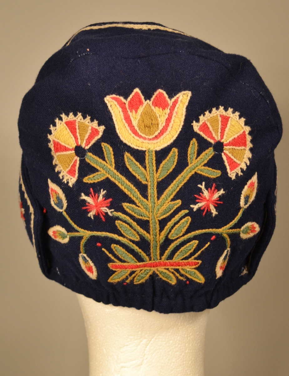 A: Bunad. Blått ullstoff, tynn klede. Har ein brodert bord 5 cm frå nedre kant. Brodert i ullgarn. Borden er 33 cm bred og går rundt same høgde. Det er en grenbord med blomster sydd i plattsøm, kontursting og franske knuter. Overdelen er eit skjørteliv. Rundt skjørtet er det brodert ein bord i kvit snorsøm, fiskebeinsting og franske knuter. Bak 3 stjerner i røde og kvite, foran på skjøtene 4 stjerner. Den broderte kvite borden fortsetter foran og opp og rundt halslinning. Foret overdel med lysgrå silke. 8 sølvringer foran i åpningen for sølvkjede. Denne bunaden har nedsydde folder frå 5 cm og opp til 8,5 cm lengde (ikkje vanleg). Splitten i skjørtet er satt saman med to trykknapper og ein hekte, og overdelen er satt saman i livet med to hekter. Skjørtet er festet til overdelen ti steder. Overdelen går i spiss ned bak.

B: Lue
Maken stoff og broderi som bunad. På pullen er det brodert eit tre med blomster. Same broderi som på overdel er brodert foran på luen. Foret med lysegrå silke. Kyse fasong. H: 17,5 cm, B:18,8 sm

C: Veske
Same stoff og broderi som bunad. Lås i messing. Same for. Låsen påsydd for hand. Låsen er merket: 
JONS KRISTIANSEN
KJOSE
NN
Veske med lås, total lengde: 28,7 cm, bredde: 16,4 cm

D: Skjorte
Kvit bomull med nuppereller. Halslinning 6 cm x 36 cm, skjorta rynket rundt halslinning. Splitt 16 cm ned midt foran. Lengde, 42 cm. Innsatt spjeld under arm 7cm x 7 cm. Vidde arm 42 cm, armlinning 6 cm x 19,5 cm. Total bredde frå arm til arm 153 cm, hvorav bolen er 52,5 cm. Innfelt skulderstykke 8,3 x 15,6 cm. Knapphull for knapper.