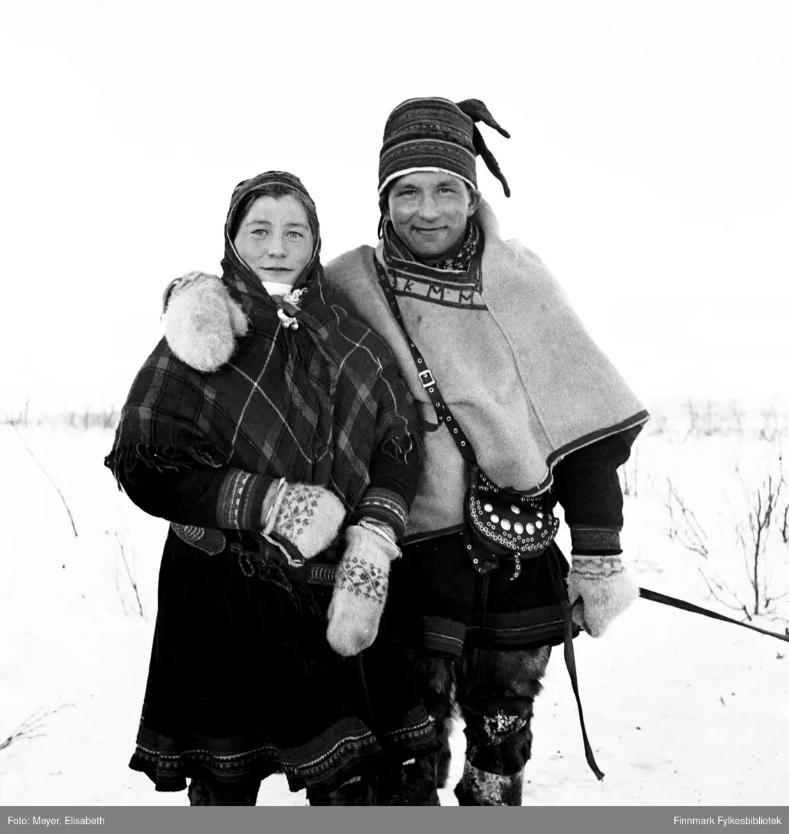 Portrett av Inga Johansdatter Sara og (antatt) Johan Klementsen Hætta. Tatt i Kautokeino i perioden 1939-1940. Begge kledd i samisk kofte, med luer, sjal og Mathis bærer også en rikt dekorert skinnveske over sin Luhkka (samisk poncho).