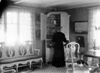 Ester Ellqvist-Bauer står i ett rum i stugan de hyrde i Torstorp utanför Gränna och tittar in i ett skåp med glas och porslin.
