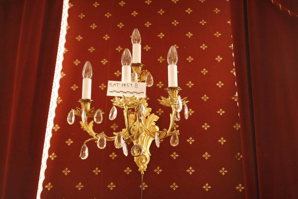 Elektrisk vegglampe med tre armer. Støpt metall. Forgyllet. Påhengte fasetterte glassdråper.