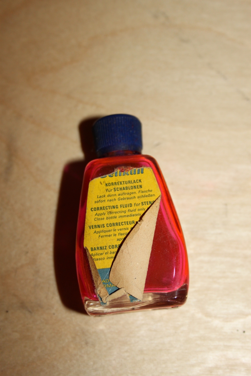 Blekkflaske med skrukork. Glassflaske med papirmerkelapp. Flasken har avrundede former/hjørner. I skrulokket er det festet en pensel.