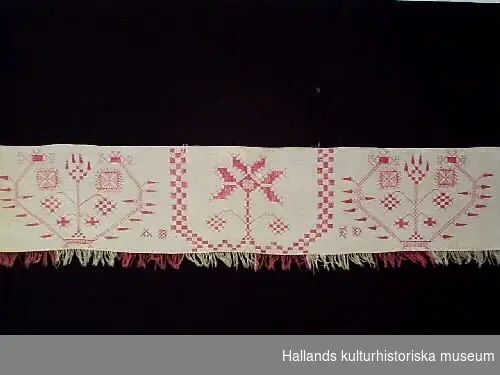 Hängkläde med frans. Vitt med broderier av bomullsgarn i rött och röd och vit frans.