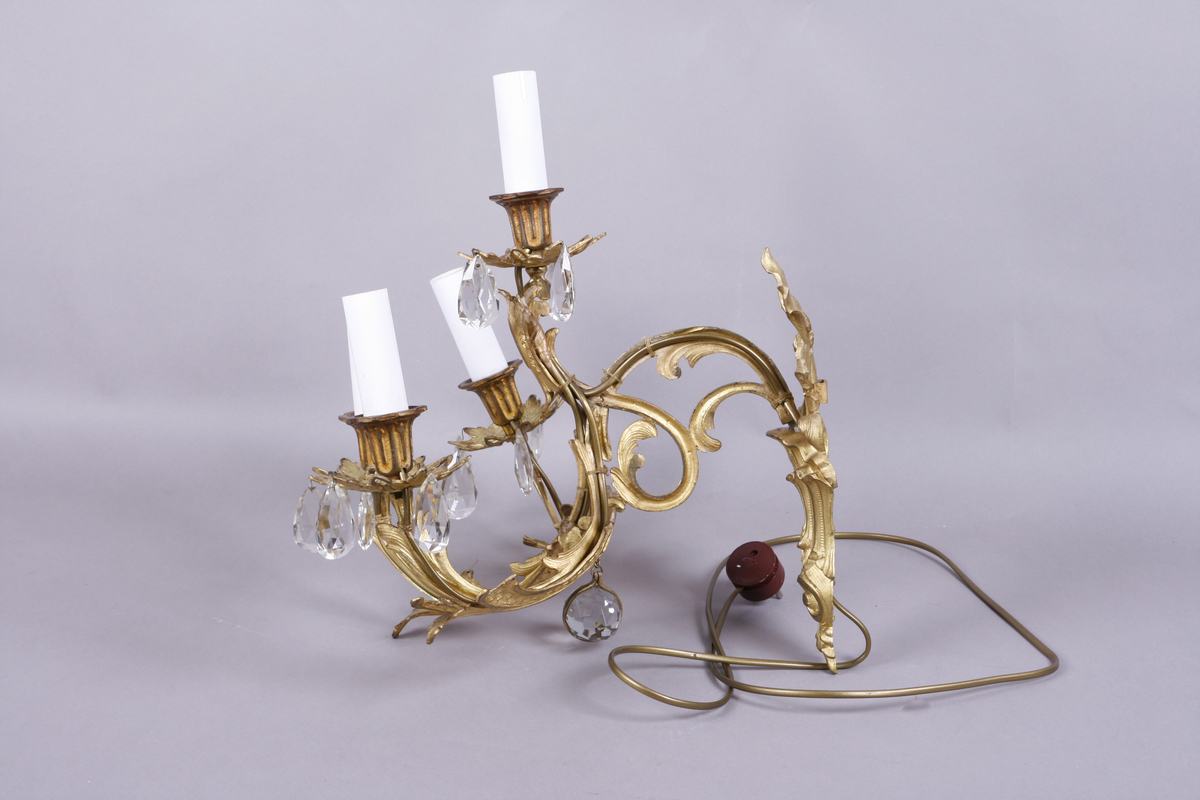 Elektrisk vegglampe med tre armer. Støpt metall. Forgyllet. Påhengte fasetterte glassdråper.