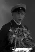 Ateljébild på en man som har tagit realexamen. Han har en blombukett och mössa. Enligt Walter Olsons journal är bilden beställd av Nils Johnsson.