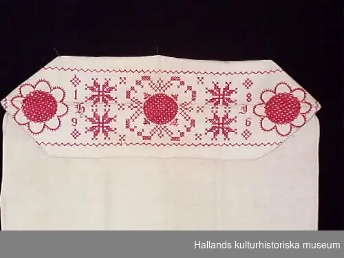 Så kallat putevar av vitt linne, broderad gavel av bomull. Broderier med rött i korsstygn: 1896 H.I.