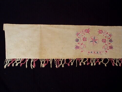 Hängkläde av bomull och linne. Knuten frans i rosa och vitt. Broderier i rosa och blått bomullsgarn. Märkt: M G E D ÅR, 1845.