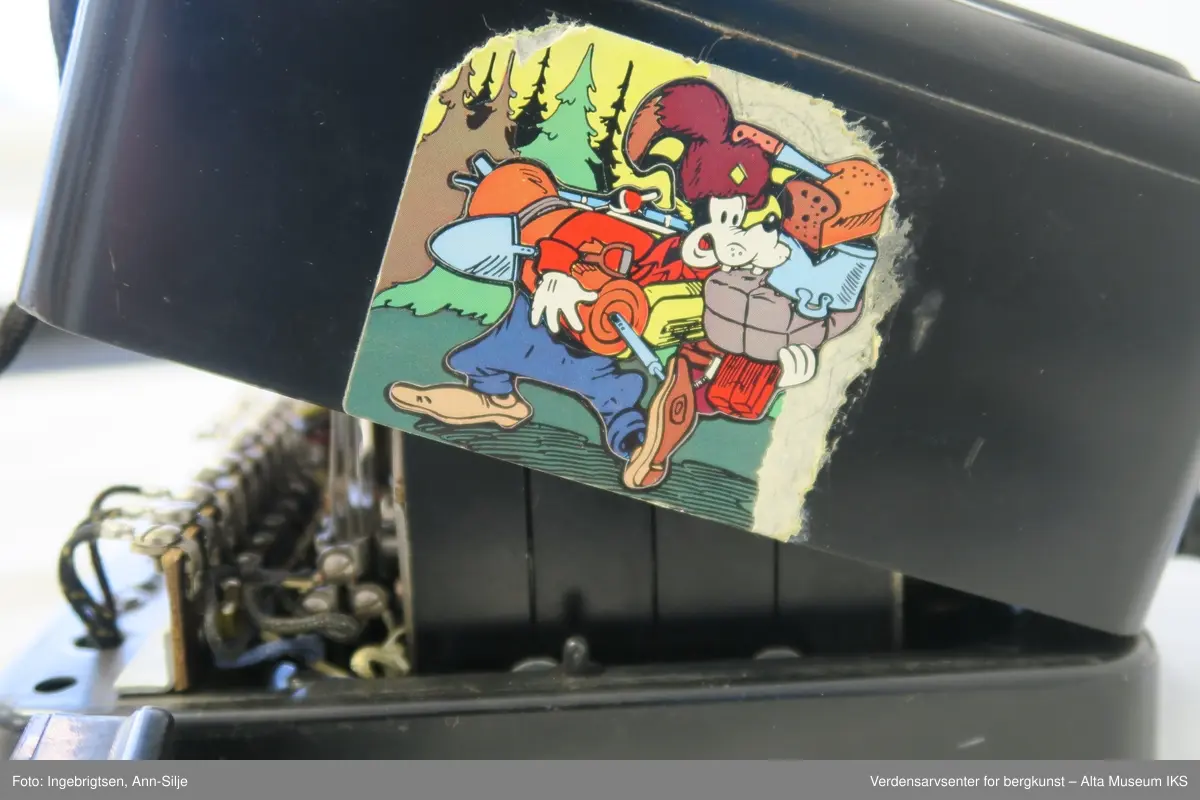 Prismeformet med bæreklo på toppen og telefonrør. Emblem med logoen til Telegrafverket på framsiden av boksen. Boksen er åpnet fra bunnen og er kilt fast slik at det ikke er mulig å lukke den. På baksiden av boksen er det et klistremerke med motiv av Langbein.