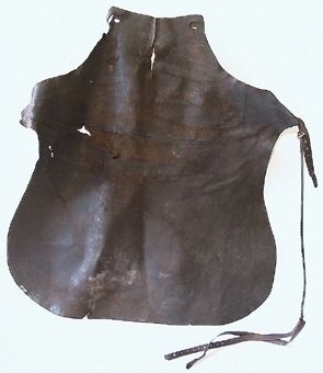 Smedförskinn av läder som är skuret i ett stycke. Skinnet har en rem runt halsen och en rem runt midjan. Spännena på remmarna är av metall.