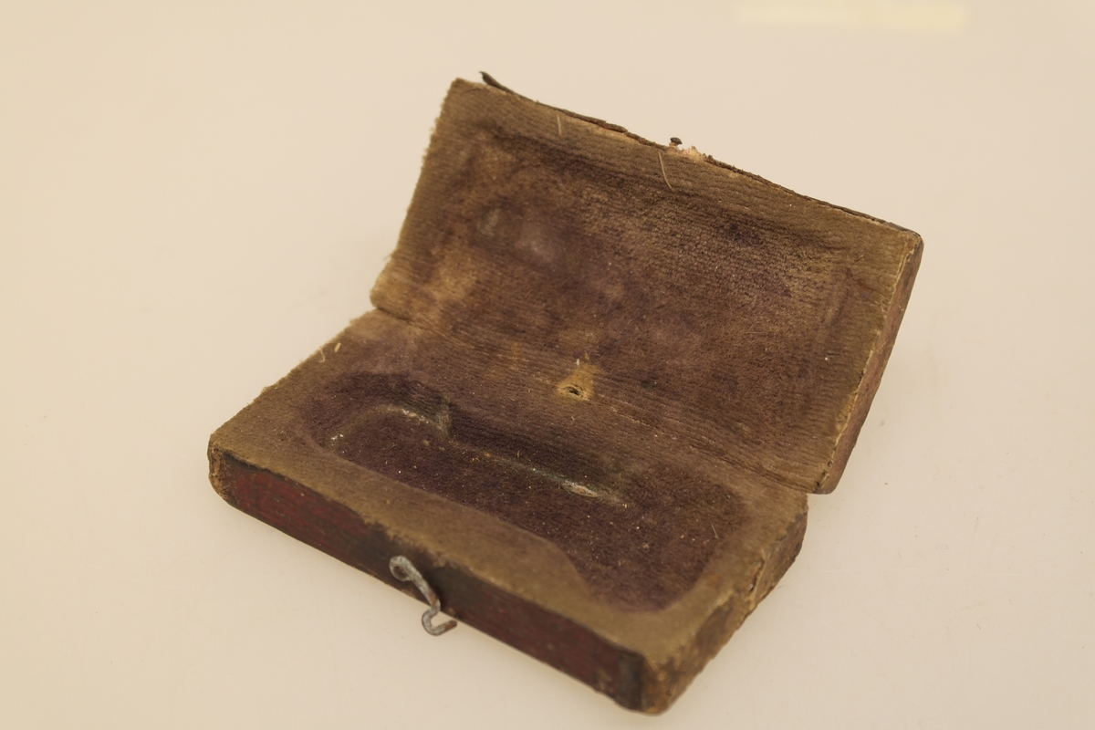 Sneppert (a) med eske (b) til bruk ved årelating. 
A) Smidd jernblad og messing. Innrissing av initialer.
B) Eske av tynt tre trukket med rødt papir utenpå og brun velour inni. Lukkes med en messinghempe.