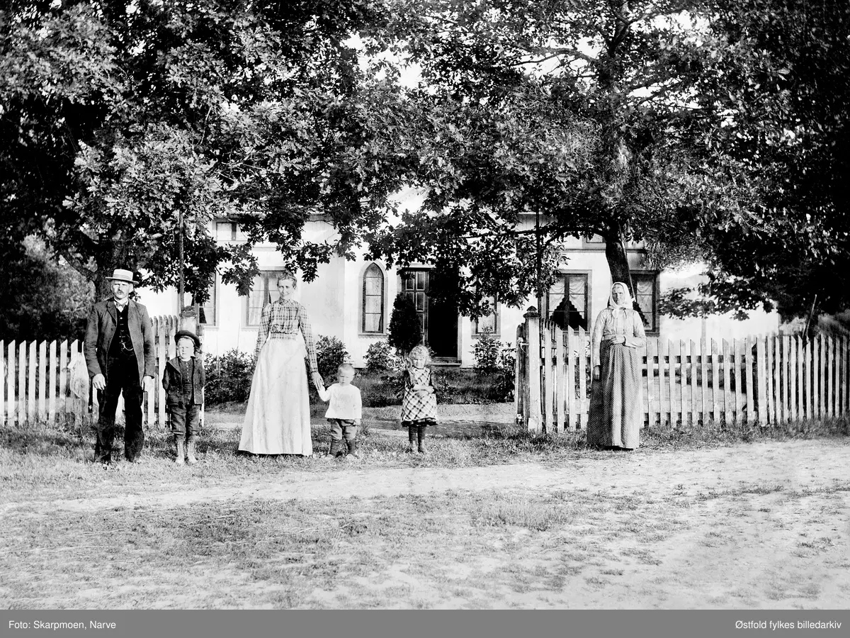 Theodor og Josefine Koppang med barn foran inngangspartiet til Nes gård, Skiptvet ca. 1902.
Fra v.: Theodor F. 1855, Osvald F. 1894, Josefine f. Schi F. 1864, Torstein F. 1899, Debora F. 1897, ant. Olaug Schie

Kommentar Morthen Auke 2017:
Den lille jenta på bildet er antakelig Debora Otilie f. 24.10.1897 gift med Jens Ludvig Skipperud d. 14.02.1980. De hadde barna Reidun, Elsa og Jens Dagfinn. Theodor var oldefar til min kone - Irene f. Koppang datter av Ola Koppang, sønn av Osvald Meyer Koppang.
Den eldre damen til høyre på bildet kan minne meg om Josefine Koppangs mor Olaug Schie. Jeg har et bilde av henne som yngre og ser en ganske stor likhet. Hun døde i 1906.
