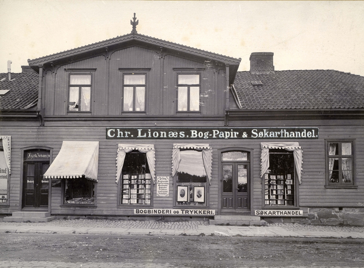 Fredrikstad. Vestsiden. Storgaten 12. Chr. Lionæs Bog-Papir og Søkarthandel.Storgaten 12. Chr. Lionæs Bog- Papir & Søkarthandel. Forretningen ble etablert 11. juli 1858 av Christopher Lionæs, overtatt av Einar Chr. Lionæs. Forretningen ble solgt til ny eier på midten av 1950-tallet.  Forretningen holdt til i alle år til Storgaten 12, men ikke i samme i bygning hele tiden. Gården på bildet ble revet tidlig på 1900-tallet for å gi plass en murgård, reist av Fredrikstad Privatbank.