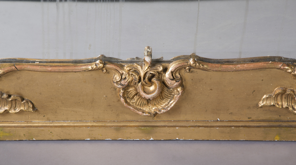 Stort, rektangulært speil med utskjæringer på rammen. Forgylt ramme. Rocailler i asymmetrisk mønster. Speilet buer seg lett ved toppstykket. Rikt asymmetrisk utskjært toppstykke med blomster og rocailler.