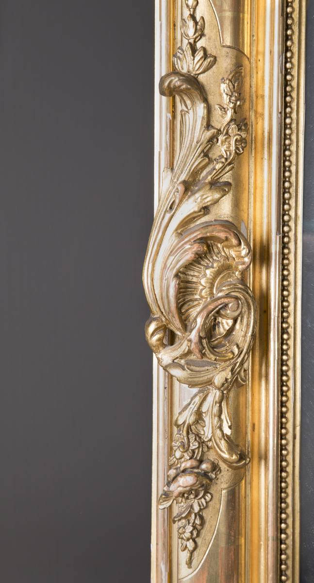 Stort, rektangulært speil med utskjæringer på rammen. Forgylt ramme. Rocailler i asymmetrisk mønster. Speilet buer seg lett ved toppstykket. Rikt asymmetrisk utskjært toppstykke med blomster og rocailler.