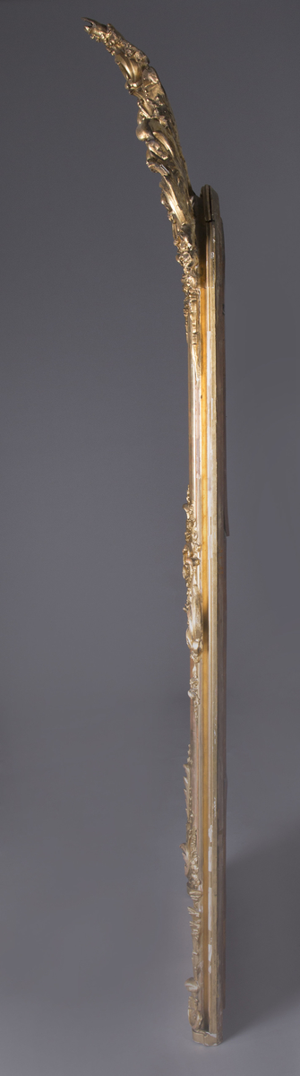 Stort, rektangulært speil med utskjæringer på rammen. Forgylt ramme. Rocailler i asymmetrisk mønster. Speilet buer seg lett ved toppstykket. Rikt asymmetrisk utskjært toppstykke med blomster og rocailler.