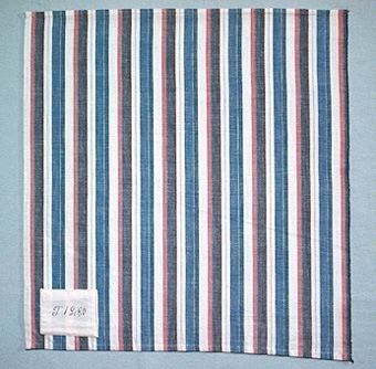 Randigt vävprov i bomullsgarn vävt i tuskaft. Varp i två nyanser blått och brunt samt oblekt, inslag i oblekt. Provet har en påsydd tygetikett med texten: "T 1280".Tygprovet är ihopfäst med ytterligare tjugoåtta prover (inv.nr 77 - 81, 83 - 100) med snören.