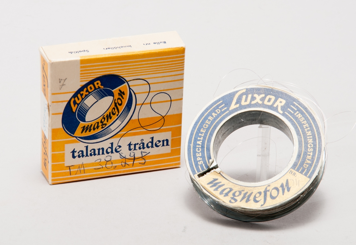 Tontråd till trådspelare, på svarvad metallspole utan etikett, märkt M 22702/60. I pappask med texten: "Luxor Magnefon, talande tråden". På medföljande pappersremsa anges: "Per Lindfors program". Spole: ytterdiameter: 70, håldiameter: 40, tjocklek: 17 mm. Kartongens längd: 80 mm, bredd: 80 mm, höjd: 20 mm.