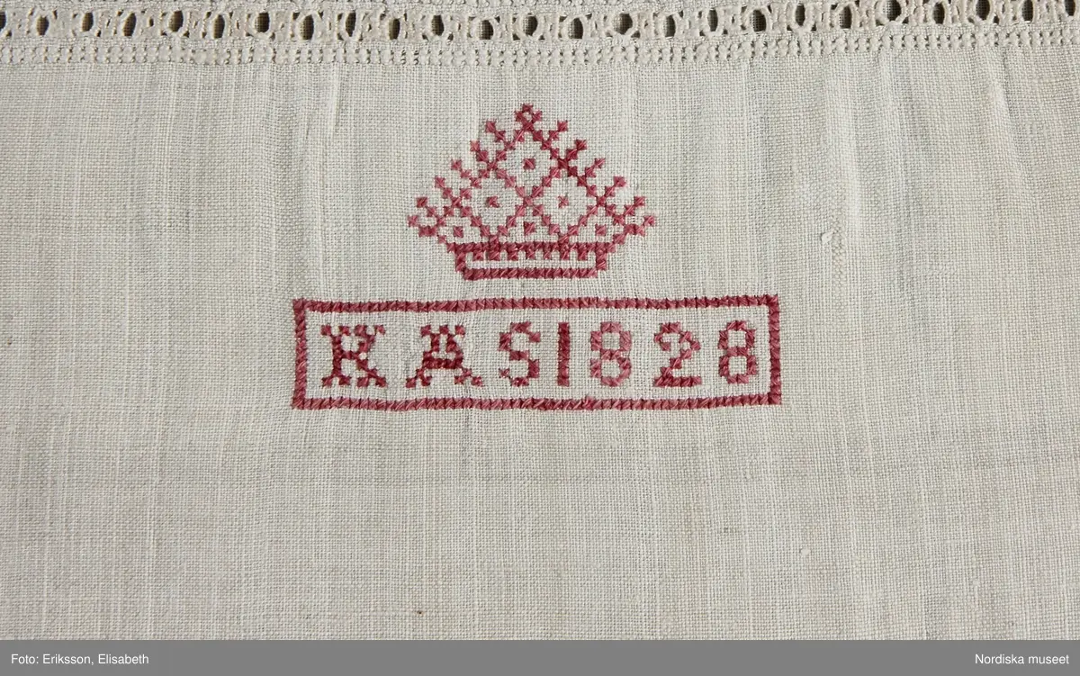 Skjorta av vit linnelärft, ett framstycke och ett bakstycke med halsspjäll som går ända ut mot ärmsömmen. Rynkad runt halsen mot hög uppstående krage kantad med knypplad 3 cm bred linnespets av tät skånsk typ. På halva kragbredden broderad bård i vitt och ljusgrått lingarn i tät utdragssöm av skånsk typ. Halssprund 25 cm långt med ändstopp av en bit s.k. vävd spets. I kragsömmen 2 stora knapphål för länkknapp se litt b.  Runt sprundet och i en kvadrat nedanför rikt broderi i utskårssöm och utdragssöm  samt något plattsöm och hopdragssöm. med vitt lingarn. Nedanför broderiet märkt K A S 1828 under "krona" med rosa bomullsgarn i korssöm. Vidsydd vid ärm med ärmspjäll, nedtill rynkad mot 3 cm bred ärmlinning med stickningar, knutar och enkel utdragssöm samt kantad med lätt rynkad knypplad spets av samma sort som på kragen, ärmsprund med 2 motstående knapphål.
En mycket typisk  brudgumsskjorta av rikaste slag från Ingelstads hd. Broderi och sömmar mycket välgjorda.
Enligt tidigare analys reovisad på katalogkortet är vävens lintråd vänsterspunnen och det går 20 varptrådar /cm, I broderiet är det högertvinnat  lingarn.
/Berit Eldvik 2010-10-15