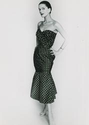 Modell i prickig klänning, halsband, klocka och sandaletter.