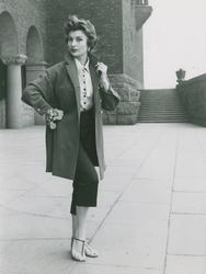 Modell i blus, jacka, capribyxor, armband och sandaler på et