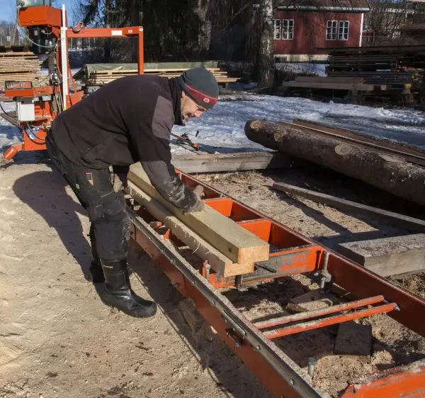 Nyskårne planker fraktes ut på et oransje stativ i enden av saga.