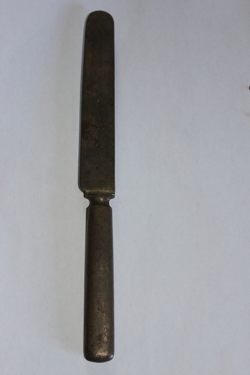 Kniv, slätt blad med rundad topp. Skaftet har oval genomskärning. Vid övergången mellan skaft och blad en vulst. Firmanamnet stämplat på bladet.