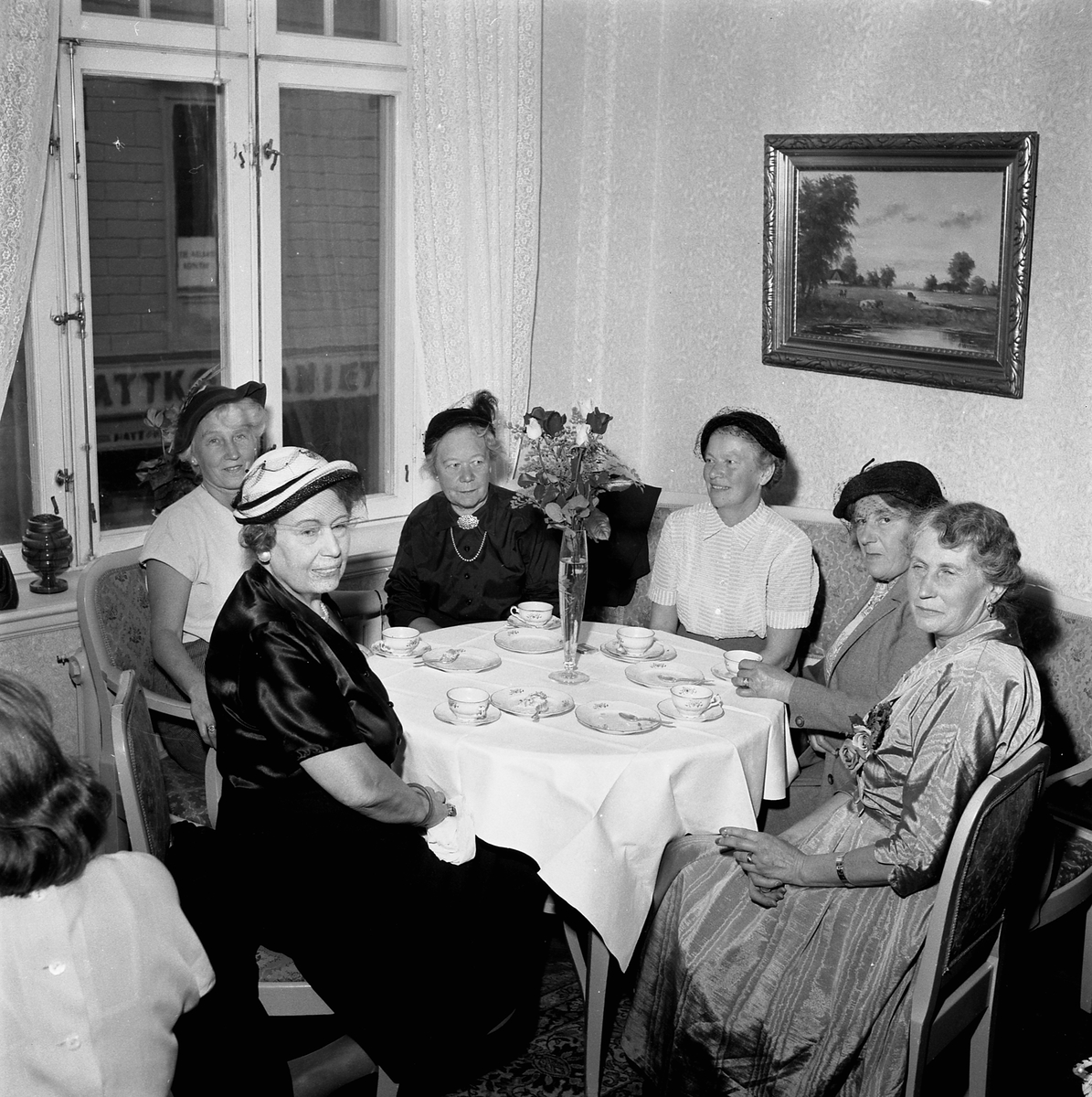 Orig. text: Fru Forsby Centralkondis.
Centralkonditoriet på Hospitalstorget. Flera kvinnor sitter runt ett bord och dricker kaffe. 
Centralpalatset ritades av arkitekten P J Pettersson i Stockholm, men byggmästaren Anders Ohlsson lät dock Axel Brunskog göra nya fasadritningar mot Stora torget. Den fasaden har därför en tydligare jugendkaraktär än vad övriga fasaden har. Byggnaden stod klar 1909.

Extern information: Fotot är taget när fru Maja Forsby, några dagar efter sin sextioårsdag den 26 september 1953, bjöd några väninnor på födelsedagskaffe. Födelsedagsbarnet sitter längst till höger iförd sidenklänning med en blomsterdekoration. I bildens förgrund sitter Celia Göransson, damen i vita blusen vid fönstret är födelsedagsbarnets syster, Inga Wennergren. Damen i svart klänning är domprostinnan Vivi Hammers. Mitt i bild sitter Lisa Thell och bredvid Maja Forsby sitter maria Elisabeth Lisa Carlson.