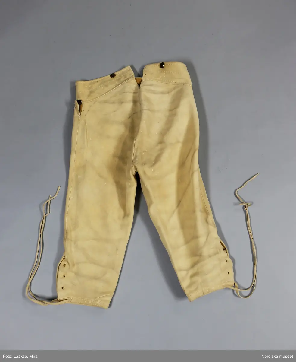 Hel mansdräkt från Österåker A.-F.

A. Hatt
B.Långrock
C.Knäbyxor
D.
E
F. Halsduk

A. Hatt, höjd 15 cm, cylinderformig av svart felb, brättet uppvikt vid sidorna och kantat med svart sidenband. Kullen något insvängd i sidorna. Kring kullen ett svart band med ett rektangulärt spänne på  vänster sida. Svettrem av rött skinn, foder av papper, tryckt med silverfärg.
B. Långrock
C. Knäbyxor längd 79 cm, av sämskat renskinn, midjegjord och smal lucka med 4 kullriga mässingsknappar, 2 fickor vid sidan om luckan. Knäsprund som knäpps med hakar och hyskor, knälinningar som knyts med smala skinnremmar.
/Berit Eldvik juni 2005
F. Halsduk, avklippt tresnibb av yllemuslin. Klippt av ett större halskläde. Grålila bottenfärg med tryckt mönster i rött, grönt och gult på utsparad vit botten, gles lila yllefrans. Fållad med tråckelstygn. Stämpel i svart i ena hörnet, svårläst men troligen: Göteborg 184?.
Viks till smal remsa, vid påtagningen läggs mitten af halsduken över strupen, ändarna tas i kors i nacken, och knyts sedan fram.
/Berit Eldvik 2010-01-08

