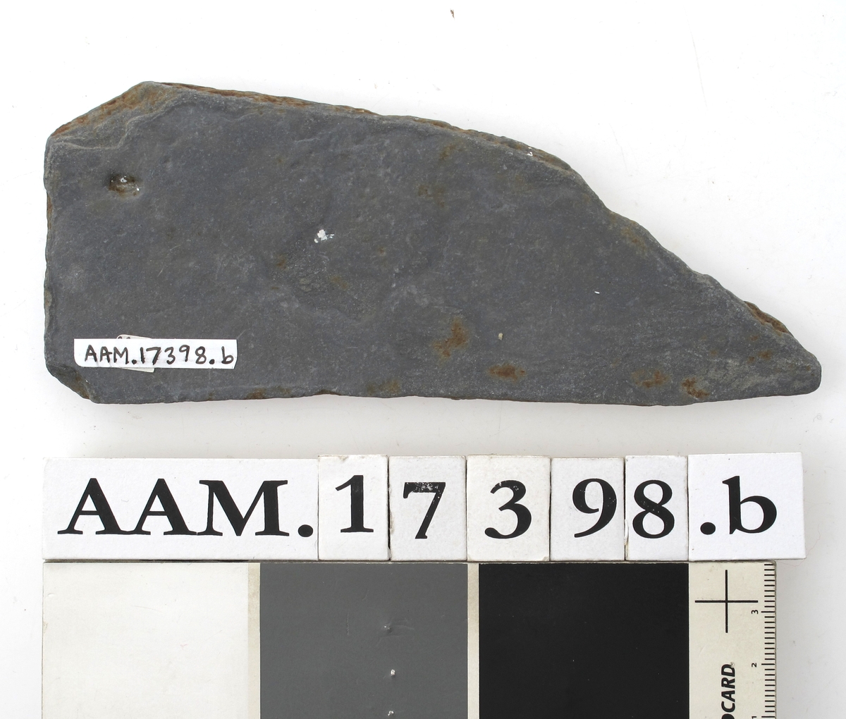 Skifertavle i fire deler .  
a)  17,7 x 8. Femkantet hjørnestykke.  
b)  15 x 6,3. Hjørnestykke med et hakk,  den lengste side er buet. A-b = G 1435.  
c)  16,5 x 5,8. Smalt spisst bladformet. = G 1153.  
d)   Lite skiferstykke. L. 4,8. B. 1,5