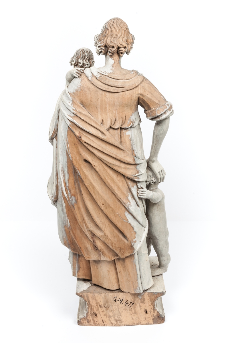 Kyrklig skulptur, trä, staty från gamla korskranket i Heliga Trefaldighets kyrka i Gävle, av Ewert Friis omkring 1665. 

Stående kvinnofigur med naket barn på vänster arm samt stående naket barn vid höger sida. Sistnämnda barn har ett brinnande hjärta i höger hand och kvinnans vänstra hand på sitt huvud. Vänster ben är främst, foten avslagen. Sittande barnets ena ben och andra fot avslagna. 
Fyrsidigt, profilerat postament. 
Gråvit färg.
