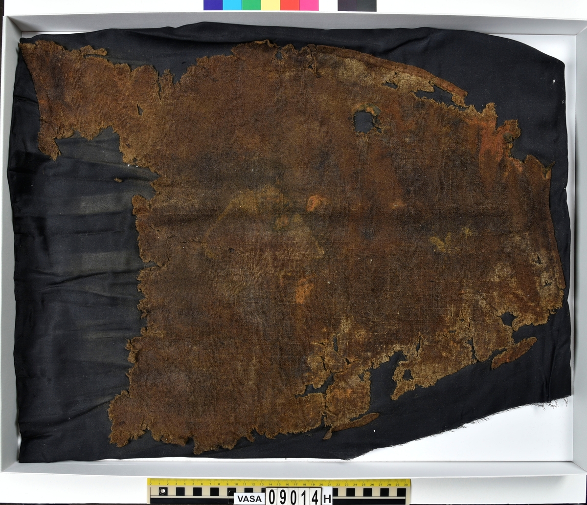 Textildokumentation 2018
Textil, fyndnumret består av mer än 50 st fragment uppdelade på 09014a-h.
Kontextgrupp ÖB20 (övriga fyndnummer i gruppen: 07732, 07762, 09228)
Relaterade fynd: Kontextgrupp ÖB17 och ÖB 18.
.
Fnr 09014a Typnr ÖB20.3:1
Sammanfattning - Ett textilfragment av ull vävt i tuskaft. Färgen är nu mörkbrun, fibrerna varierar i färg vilket tyder på att det är naturfärgad ull. Fibrerna är i vissa partier skadade på ytan och ser därför vita ut. Väven är tunn, jämn och fin och har inga spår av ytbehandling. Fragmentet har tre tillskurna kanter, två av dessa har spår av tre olika sömmar (söm 1: kvicksöm/förstygn). Formen tyder på att det är ett skört till en tröja. Andra delar: Jämför med 07726. 
.
Fnr 09014a Typnr ÖB20.4:1
Sammanfattning - Ett textilfragment av ull vävt i tuskaft. Färgen är nu mörkbrun, originalfärg okänd. I mikroskop ser tyget blåsvart ut. Väven är mycket jämn och slät. I sömsmånen på sida A finns bevarad lugg, på sida B är luggen så välbevarad att bindningen inte syns. Fragmentet har två tillskurna kanter med hål och avtryck av sömmar, även trådrester finns (söm 1: kaststygn - fälld kant, söm 2: ev förstygn - sammanfogande, söm 3: kaststygn - fälld kant). På sida B finns blåfärgad ull och silkesfibrer. 
.
Fnr 09014a Typnr ÖB20.5:1
Sammanfattning - Ett textilfragment av ull vävt i tuskaft. Väven är jämn och tät. En av kanterna är troligen tillskuren, inga sömrester finns. Tyget har inga spår av ytbehandling. På ytan finns en del bastfibrer. Relaterade fynd: Vävens struktur liknar ÖB20.4:1 men tygerna har ändå olika karaktär och detta fragment saknar lugg. 
.
Fnr 09014a Typnr ÖB20.6:1
Sammanfattning - Ett textilfragment av ull vävt i tuskaft. Färgen är nu brun, originalfärg är okänd men möjligen naturfärgad, fibrerna är mycket släta och varierar i färg från brun till nästan svart. Fragmentet är litet och mycket skadat, endast några få bindepunkter återstår vilket försvårar mätningar. 
.
Fnr 09014a Typnr ÖB20.7:1
Sammanfattning - Ett textilfragment av  ull vävt i tuskaft. Färgen är svartbrun, originalfärg okänd men möjligen naturfärgad då fibrernas färg varierar. Inga tydliga spår av ytbehandling. Väven är jämn men garnet är hårt spunnet vilket ger tyget en kypertkaraktär (falsk kypert). Fragmentet har inga tillskurna kanter eller sömmar. På ytan finns enstaka vita silkesfibrer.
.
Fnr 09014a Typnr ÖB20.8:1
Sammanfattning - Ett textilfragment av ull. Fragmentet är mycket litet och dåligt bevarat så bindningen är svår att avgöra, troligen 2/2 kypert. Färgen är svart, möjligen naturfärgad ull då fibrerna varierar något i färg. Tyget har ingen synlig ytbehandling. Garnet är hårt spunnet vilket ger tyget en speciell karaktär. 
.
Fnr 09014b Typnr ÖB17.1:8-11
Sammanfattning - Fyra textilfragment av ull vävt i tuskaft. Färgen är mörkbrun, originalfärg okänd men den bruna tonen slår mot röd. Tre av fragmenten har tillskurna kanter och spår av sömmar. Andra delar, som troligen kommer från samma tröja, är fnr 03261a och d, 09014h samt 09228a. 
Fragment ÖB17.1:9 - Fragmentet har två tillskurna kanter varav den ena har spår av en söm. Fragmentet är troligen sidostycket till en tröja. Den tillskurna kanten har då varit monterad mot tröjans bakstycke och bör ha hört samman med fyndnummer 03261d, vilket är ett bakstycke till en tröja.
Fragment ÖB17.1:10 - Fragmentet är mycket skadat men är troligen av typen ÖB17.1. Formen är densamma som för del av fragment ÖB17.1:9 och kan därför vara en dubblering av detsamma, alternativt det motstående sidostycket.
.
Fnr 09014c Typnr ÖB20.9:1-19
Sammanfattning - Nitton textilfragment av ull vävt i tuskaft. Färgen är brun, originalfärg okänd. Sida B har en kort tät lugg som döljer bindningen. På sida A finns ingen lugg och bindningen är synlig. Fjorton av fragmenten har tillskurna kanter och sömmar. Tre av fragmenten har sydda knapphål. Flera fragment är dräktdelar, till exempel finns en fragmentarisk krage. På ytan på flertalet fragment finns fibrer i flera klara färger, till exempel rosa, röd och blå. Vita fibrer finns i stor mängd, kan vara recenta.

Fragment ÖB20.9:1 - Fragmentet har flera tillskurna kanter med avtryck och hål efter olika typer av sömmar (söm 1: ev. sammanfogande, söm 2: kaststygn - fåll, söm 3: kaststygn - sammanfogande, söm 4: kaststygn - sammanfogande, söm 5: osäkert, söm 6: osäkert), trådrester finns. Kanterna och sömmarnas karaktär gör att sida A bedöms vara plaggets rätsida/utsida. Några hål som ej är stygnhål men kan vara original finns. I fragmentet sitter fast två stycken silkestrådar (söm 7: silkestråd med knut, fäst i tyget, söm 8:  silkestråd med ögla, fäst i tyget). Det är samma typ av tråd som knapphålen på fragment ÖB20.9:2 är sydda med. På sida A finns ett område med extra mycket korrosion och även en långsmal vitaktig avlagring.

Fragment ÖB20.9:2 - Fragmentet har inga bevarade tillskurna kanter, dock finns en någorlunda välbevarad rad med knapphål. Samtliga knapphål är trasiga i ena sidan så deras ursprungliga storlek går ej att avgöra. Knapphålen är sydda med knapphålsstygn i silkestråd och sitter med 13-15 mm mellanrum (c/c mått). Det tvärställda tränsen består av ca 10 stygn och syns ej på sida B, tränsens knutar sitter vända från knapphålet. På sida B anas rester av bastfiber under knapphålsstygnen, troligen från en dubblering av tyget eller ett foder. 

Fragment ÖB20.9:3 - Fragmentet har fyra stycken knapphål, varav ett är helt. Knapphålen är skurna på skrådden. Eventuellt finns spår av en söm längs en del av kanten. Knapphålsstygn och trådrester är mycket fragmentariska.

Fragment ÖB20.9:4 - Fragmentet har tre stycken knapphål.  Knapphålen är sydda med knapphålsstygn i silkestråd. Knapphålens längd är 19-20 mm och de sitter med 18-22 mm mellanrum (c/c mått). Eventuellt är fragmentets ena kant en sömsmån, kan ha varit monterad mellan andra tyglager (kanten har avvikande färg). Under knapphålsstygnen på sida B finns rester av annat material, eventuellt bastfiber. Bastfibrer finns också utspridda över ytan på sida B, kan vara rester av en dubblering till tyget eller ett foder, se fragment 9:2. På sida A finns avlagringar och korrosion. 

Fragment ÖB20.9:5 - Fragmentet har bristningar i tyget som ser ut som knapphål, dock finns inga rester av stygnhål eller tråd. Fragmentets ena kant är troligen en sömsmån, kan ha varit monterad mellan andra tyglager (kanten har avvikande färg). Enstaka spår av söm och tråd finns längs kanten (söm 1), dessa är mycket otydliga. På fragmentets andra (mycket trasiga) kant finns ett mycket tydligt stygnhål. Fragment 9:4 och 9:5 ser ut att kunna höra ihop, dock går trådsystemen åt olika håll så det är inte fallet.

Fragment 9:6-9 - Till det stora fragmentet 9:6 hör det lilla lösa fragmentet 9:7. I fragment 9:6 sitter två fragment fastsydda, 9:8 och 9:9. De sammansydda fragmenten har tre tillskurna kanter och spår av minst fem sömmar (söm 1: kaststygn, söm 2: förstygn el. liknande - sammanfogande, söm 3: kaststygn, söm 4: sammanfogande, fäster ihop 9:6 med 9:8 och 9:9, söm 5: två stygnhål), trådrester finns. Det är troligt att 9:8 och 9:9 är delar av samma tillskurna bit, och att den utgjort en dubblering till 9:6 (inklusive 9:7). Den tillskurna formen ser ut att vara en krage. Fragmentet skulle då vara en halv krage, bevarad från framkant till nästan mitt bak. På sida A finns en beläggning på delar av ytan. På sida B finns en mängd fibrer i klara färger: blå, vit, rosa, tegelröd, orange, karminröd, grön, mörkgul och grå. fibrerna ligger ytligt med nästan samtliga sitter delvis fast i tygets lugg eller har en eller båda ändar nere i vävens bindning. Fibrerna bör därför vara ursprungliga. Sida A har en mindre mängd av nämnda fibrer, mest förekommande på ytan av fragment 9:8 och 9:9.

Fragment ÖB20.9:10 - Fragmentet har två tillskurna kanter. Dessa är invikta mot sida B som en 6-7 mm bred fåll som är fastsydd med kaststygn, trådrester finns (söm 1 och 2). Fragmentet kan vara ett skört till en tröja. På båda sidors yta finns fibrer i klara färger: grå, ljusblå, orange, orangebrun, vitgul, blå svart, vit, röd, korallröd och rosa.

Fragment ÖB20.9:11 - Fragmentet har tre tillskurna kanter med sömmar. Två av kanterna är invikta och fastsydda mot sida B, som fållar (söm1: kaststygn - fåll, söm 2: kaststygn - fåll). Stygnen går ej igenom till sida A men sömmen syns som bucklor i fragmentets yta. Söm 3 längs den tredje kanten har troligen varit en sammanfogande söm sydd med kaststygn. Stygn och trådrester finns bevarade från samtliga sömmar. Under fållen vid söm 1 finns ett litet fragment av en annan textiltyp. Troligen ursprungligen en dubblering eller liknande. Fragmentet är ca 10x5 mm stort och har fått typnummer ÖB20.16:1. På ytan på sida B finns enstaka bastfibrer.

Fragment ÖB20.9:12 - Fragmentet har två tillskurna kanter med sömmar (söm 1: ev kaststygn, söm 2: osäker). Vid söm 2 är sömsmånen vikt mot sida B. Vid söm 1 är kanten inte vikt. Fragmentet har samma form som ÖB20.9:6, "kragen".

Fragment ÖB20.9:13 - Fragmentet har två tillskurna kanter med sömmar (söm1: sammanfogande, söm 2: osäkert). De två övriga kanterna är eventuellt också de tillskurna men spår av eventuella sömmar är för otydliga. Enstaka fibrer med klara färger (rosa, blå, vit) finns på båda sidor, fler på sida B. Vid söm 2 finns på ett ställe en fiberknippa som kommer upp ur vävens bindning, kan vara rester av en tråd och är eventuellt halsplat silke. 

Fragment ÖB20.9:14 - Fragmentet har en tillskuren kant med söm (söm1: ev sammanfogande). I stygnhålen finns rester av tråd.
.
Fnr 09014c Typnr ÖB20.10:1
Sammanfattning - Ett textilfragment av ull vävt i tuskaft. Färgen är brun, originalfärg okänd. Sida B har en kort och tät lugg, bindningen syns bara på sida A. Längs ena kanten finns tre stycken tydliga hål. Hålen är gjorda med ett verktyg som skär av fibrerna snarare än tränger undan dem.
.
Fnr 09014c Typnr ÖB20.16:1
Sammanfattning - Fragmentet är mycket litet och sitter inuti den invikta fållen på fragment 09014c ÖB20.9:11, det sticker bara fram någon millimeter. Fragmentet är mycket skört. Bevarandegrad och storlek gör mätningar svåra. Det är olika garn i trs 1 och trs 2. Sida B är täckt av en lugg, på sida A syns bindningen, om än fragmentariskt.
.
Fnr 09014d Typnr ÖB18.16:2-8
Ej dokumenterad
.
Fnr 09014d Typnr ÖB20.11:1-2
Ej dokumenterad
.
Fnr 09014e Typnr ÖB20.12:1-4
Sammanfattning - Fyra textilfragment av ull vävt i tuskaft. Färgen är brun med inslag av täckhårsfibrer i en mörkare brun färg, originalfärg okänd. Fragmenten är mycket fragmentariska med trs 1 bättre bevarat än trs 2. Enbart på en del av fragment ÖB20.12:1 finns trs 2 samt bindningen bevarad. Utspridda över tygets yta finns grova bastfibrer samt korrosionsfläckar. 
.
Fnr 09014f Typnr ÖB20.13:1
Sammanfattning - Ett textilfragment av ull vävt tuskaft. Färgen är mörkbrun, fibrerna varierar mellan ljus och mörk brun. Originalfärg okänd, möjligen naturfärgad ull. Garnet är hårt spunnet vilket ger väven en särskild karaktär, sida A har en mer strukturerad ytan än sida B. Fragmentet har inga tillskurna kanter. På sida A finns enstaka röda och gulgröna silkesfibrer, samt bastfibrer. På sida B finns enstaka blå, vita och rosa silkesfibrer.
.
Fnr 09014g Typnr ÖB20.14:1-3
Sammanfattning - Tre textilfragment av ull och bastfiber vävt i tuskaft. Färgen är beige för bastfibern (trs 1) och svartblå för ullen (trs 2). Trs 2 är mycker grövre än trs 1. Trs 1 är nästan helt försvunnet. Två av fragmenten har tillskurna kanter och ett har spår av en sömsmån. På ytan av fragmenten finns en stor mängd bastfiber samt en vit/rosa tuss med silke. På fragment 14:2 finns några intensivt blå ullfibrer.
.
Fnr 09014h Typnr ÖB17.1:12-13
Sammanfattning - Två textilfragment av ull vävt i tuskaft. Färgen är brun, originalfärg okänd. Det större fragmentet är tillskuret och har spår av sömmar. Fragmentet är en ensömsärm med sömmen placerad mitt bak på ärmen. På ytan finns stora rostfläckar. Andra delar: Hör troligen (trots färgskillnad) till skelettet Beatas tröja, se fnr 03261a-d, 09228a, 09014b och h.