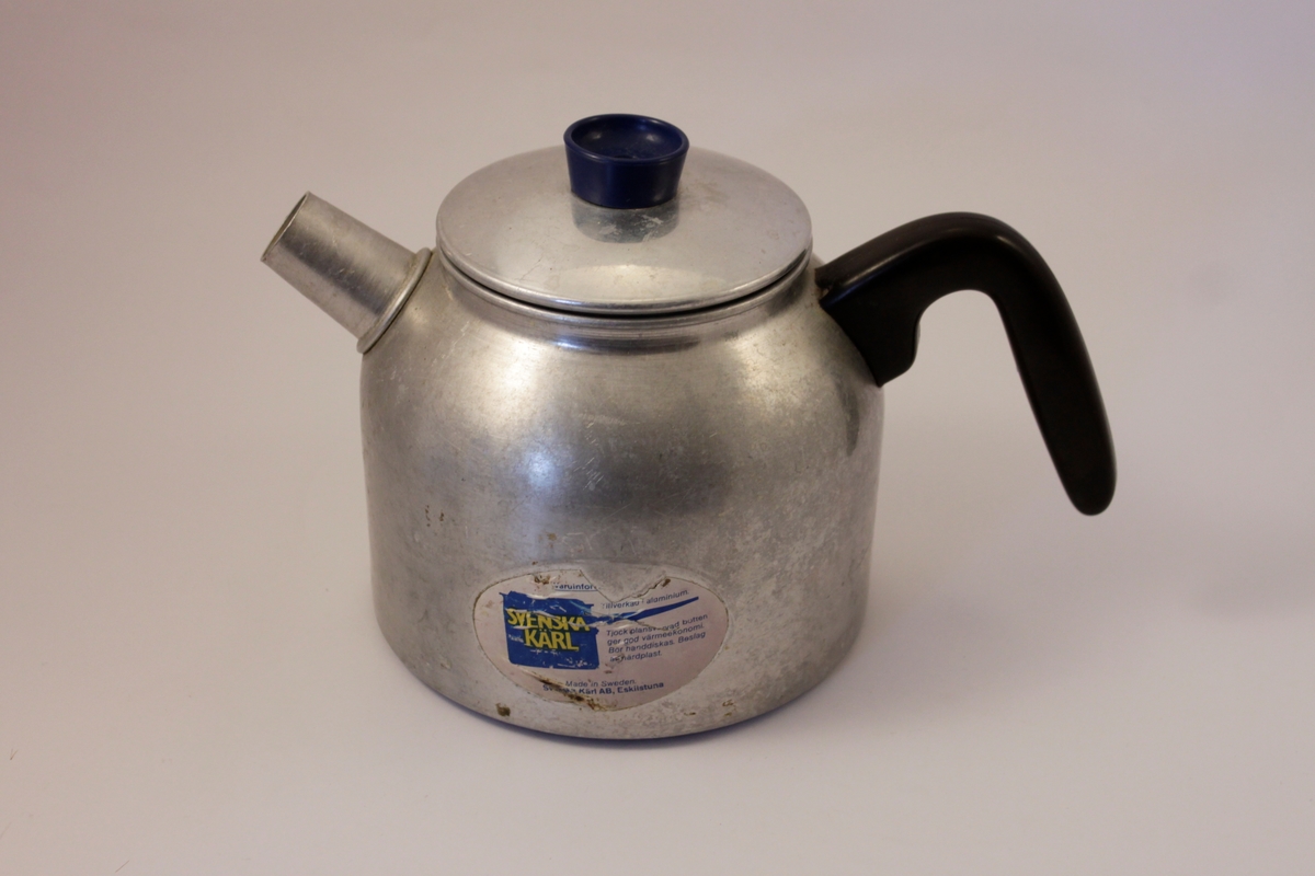 Två kaffepannor i aluminium med kort pip samt svart plasthandtag- Locket har en svart plastknopp. På sidan av den ena finns en etikett med företagsnamn och annan information.